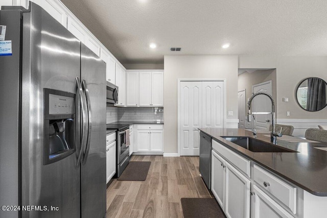 kitchen featuring light wood-type flooring, decorative backsplash, appliances with stainless steel finishes, an island with sink, and sink