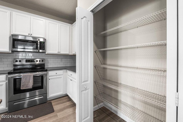 kitchen with tasteful backsplash, stainless steel appliances, wood-type flooring, and white cabinets