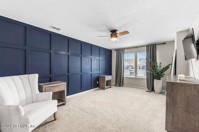 living area with ceiling fan, a textured ceiling, and light colored carpet