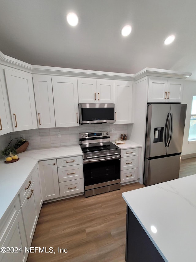 kitchen with appliances with stainless steel finishes, decorative backsplash, white cabinets, and light hardwood / wood-style floors