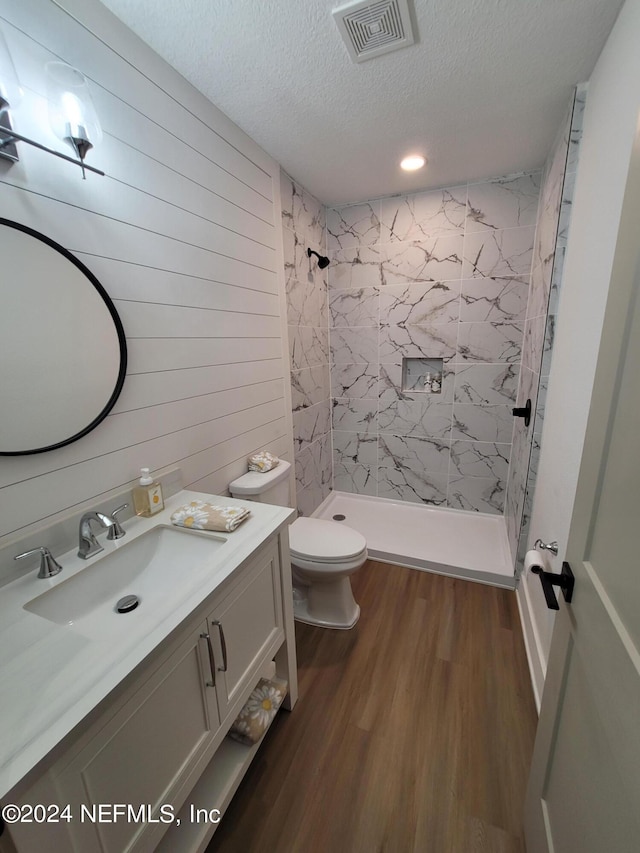 bathroom with a textured ceiling, wooden walls, a tile shower, and hardwood / wood-style flooring