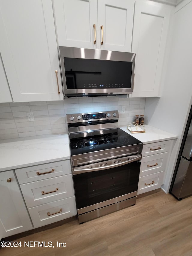 kitchen with appliances with stainless steel finishes, light hardwood / wood-style flooring, decorative backsplash, and white cabinetry