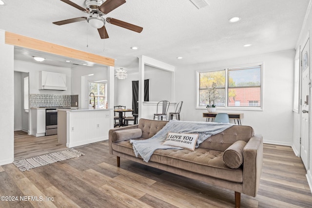 living area with light wood-style flooring, baseboards, a textured ceiling, and recessed lighting