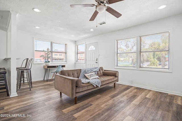 living area with a textured ceiling, wood finished floors, visible vents, and baseboards