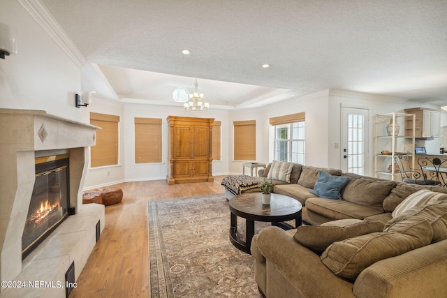 living room featuring crown molding, light hardwood / wood-style flooring, a tiled fireplace, a raised ceiling, and a chandelier