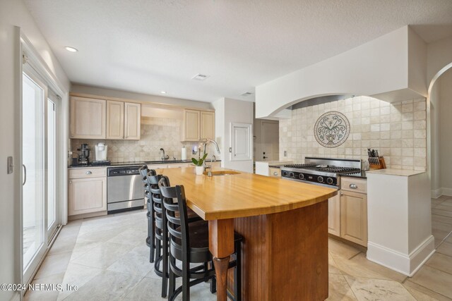 kitchen with sink, wooden counters, a center island with sink, light brown cabinets, and stainless steel dishwasher