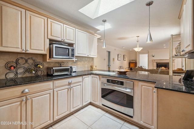 kitchen with stainless steel appliances, kitchen peninsula, dark stone counters, and decorative light fixtures