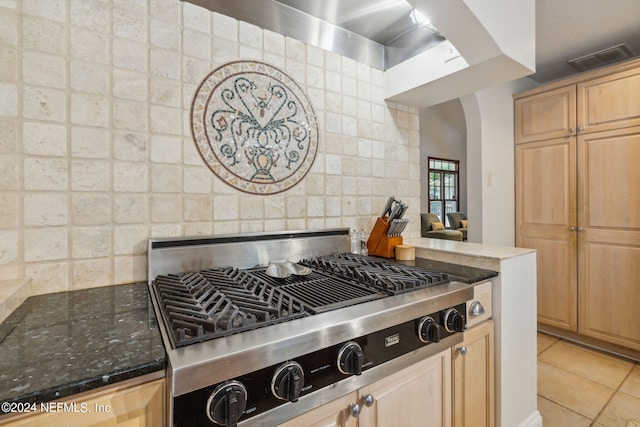 kitchen featuring stainless steel gas stovetop, tasteful backsplash, light brown cabinetry, and dark stone counters