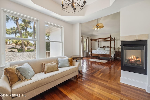 bedroom with a notable chandelier, hardwood / wood-style flooring, a raised ceiling, and a multi sided fireplace