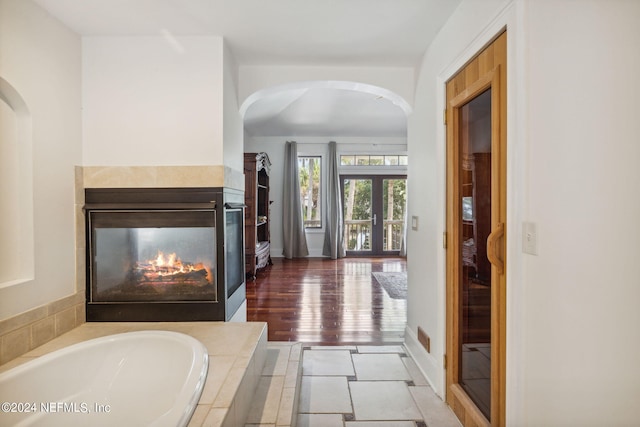 bathroom with hardwood / wood-style floors, tiled bath, french doors, and a multi sided fireplace