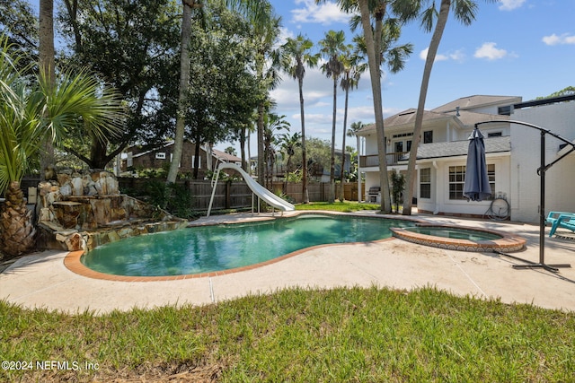 view of pool with a water slide, a patio area, and an in ground hot tub