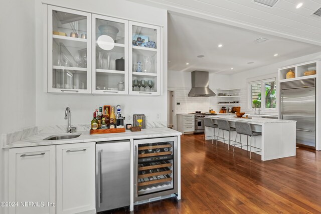 bar with high end appliances, white cabinetry, wine cooler, dark hardwood / wood-style flooring, and wall chimney exhaust hood