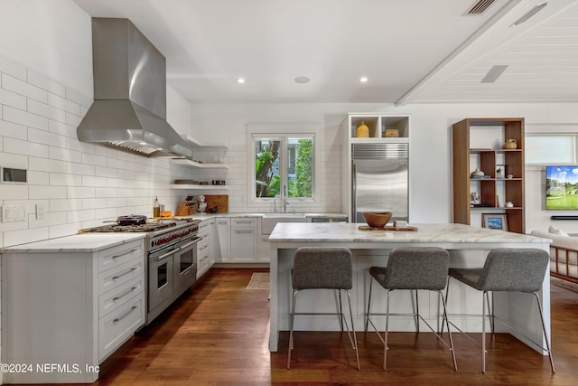 kitchen featuring a kitchen island, high quality appliances, dark wood-type flooring, wall chimney range hood, and white cabinets