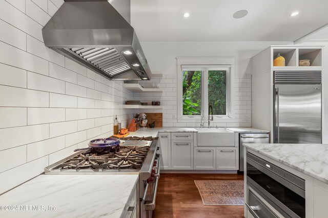 kitchen with white cabinets, sink, wall chimney range hood, premium appliances, and dark wood-type flooring