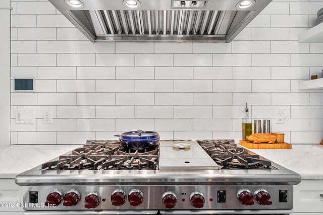 room details featuring wall chimney exhaust hood, stainless steel range, light stone counters, and white cabinets