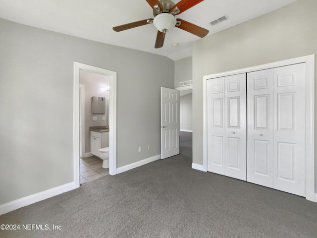 unfurnished bedroom featuring lofted ceiling, ensuite bath, dark carpet, a closet, and ceiling fan