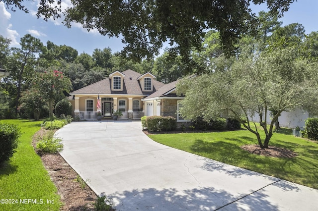 cape cod home featuring driveway, covered porch, stone siding, and a front yard