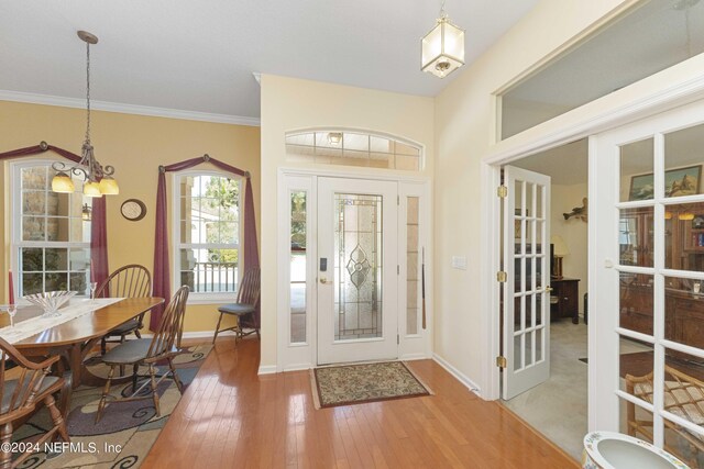 foyer with a notable chandelier, crown molding, hardwood / wood-style floors, and french doors