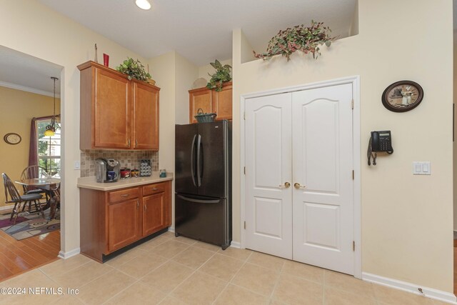 kitchen with light wood-type flooring, crown molding, tasteful backsplash, and black fridge