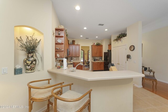 kitchen with a kitchen breakfast bar, tasteful backsplash, light tile patterned floors, kitchen peninsula, and black refrigerator