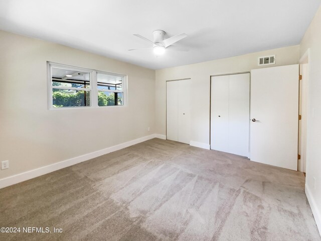 unfurnished bedroom featuring multiple closets, light colored carpet, and ceiling fan