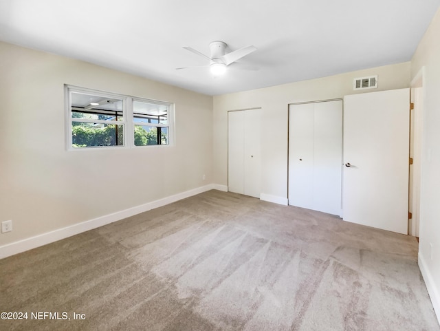 unfurnished bedroom with light carpet, ceiling fan, and two closets