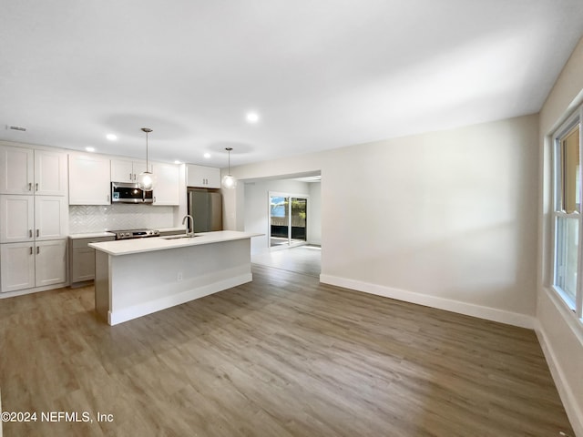 kitchen featuring wood-type flooring, stainless steel appliances, decorative backsplash, pendant lighting, and a kitchen island with sink