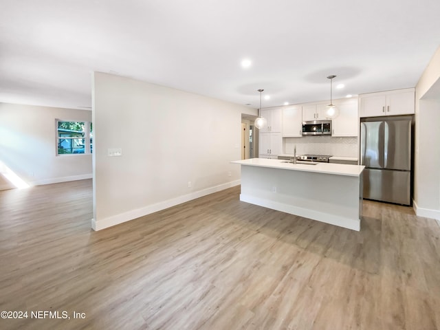 kitchen featuring backsplash, white cabinetry, stainless steel appliances, hanging light fixtures, and a kitchen island with sink