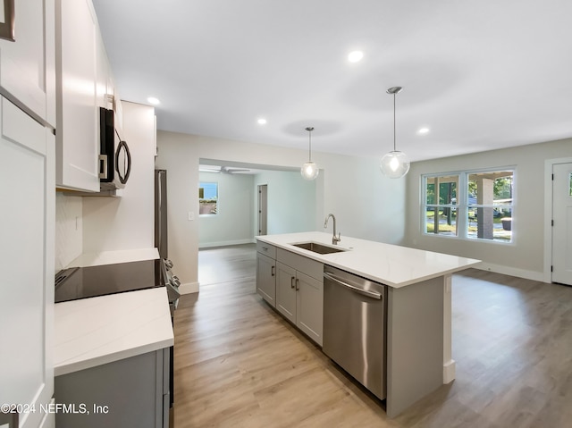 kitchen featuring sink, pendant lighting, stainless steel appliances, gray cabinets, and an island with sink