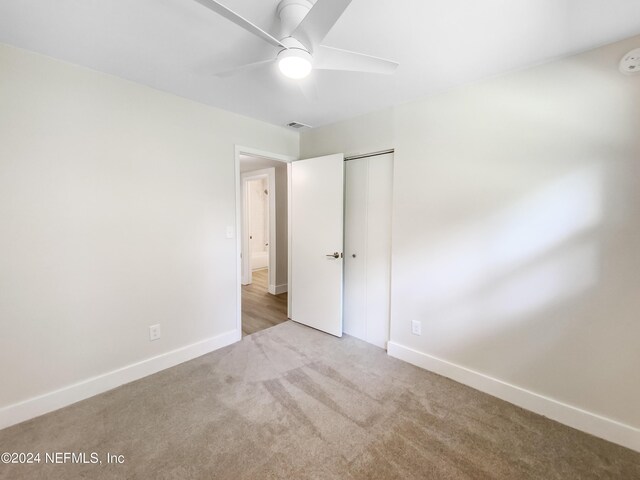 unfurnished bedroom featuring ceiling fan, a closet, and light colored carpet