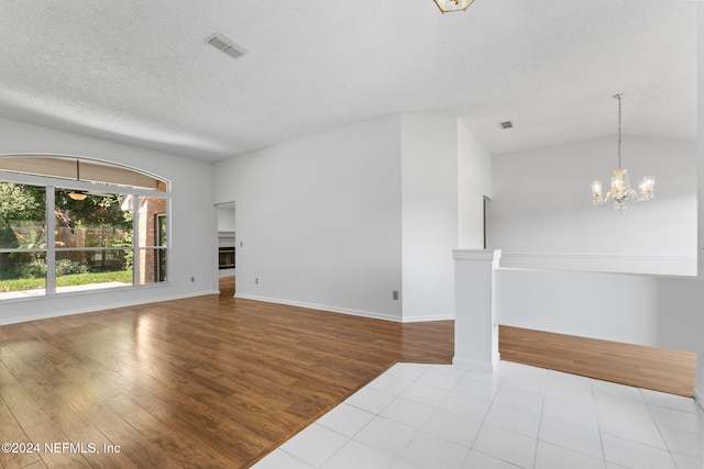 unfurnished living room with a textured ceiling, wood finished floors, visible vents, and an inviting chandelier