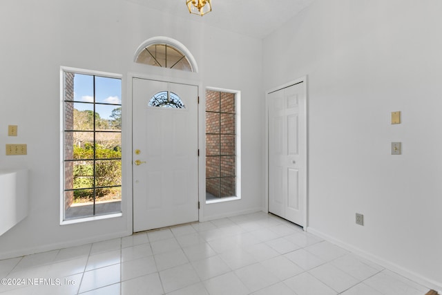 tiled foyer featuring baseboards, a towering ceiling, and a healthy amount of sunlight