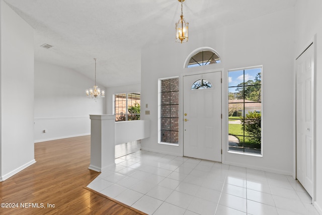 entryway with a chandelier, lofted ceiling, wood finished floors, visible vents, and baseboards