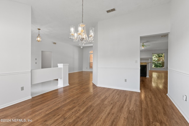 empty room with baseboards, visible vents, wood finished floors, a fireplace, and ceiling fan with notable chandelier