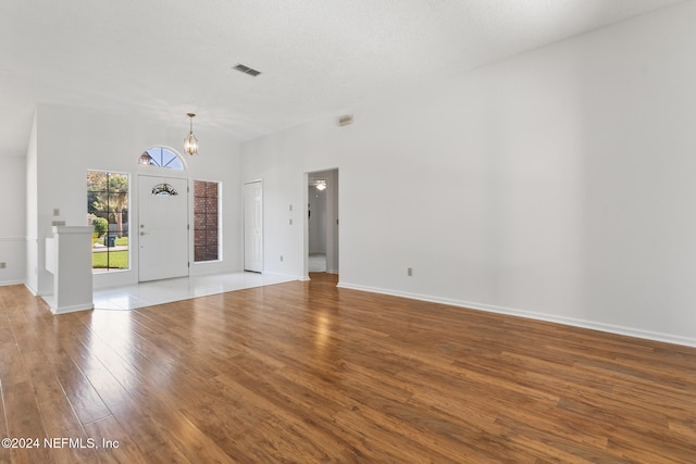 unfurnished living room featuring a chandelier, wood finished floors, visible vents, and baseboards