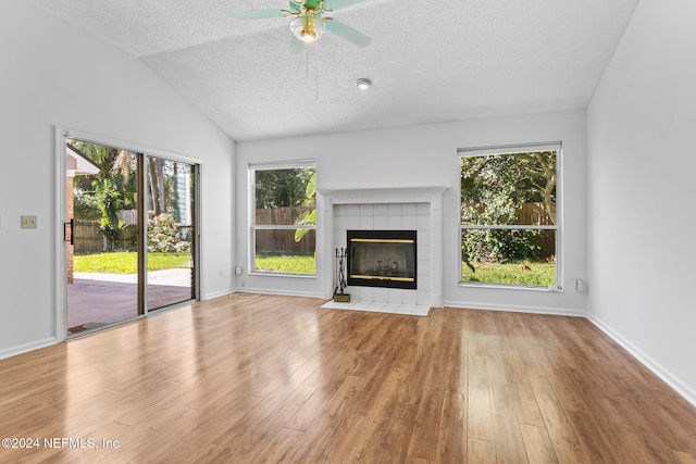 unfurnished living room featuring a textured ceiling, a tile fireplace, wood finished floors, baseboards, and vaulted ceiling