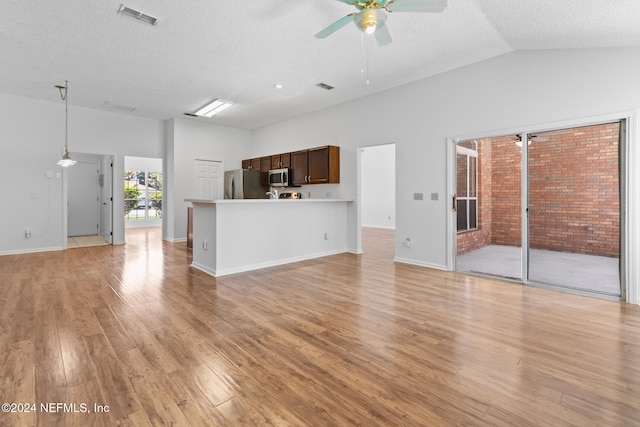 unfurnished living room with ceiling fan, a textured ceiling, visible vents, vaulted ceiling, and light wood finished floors