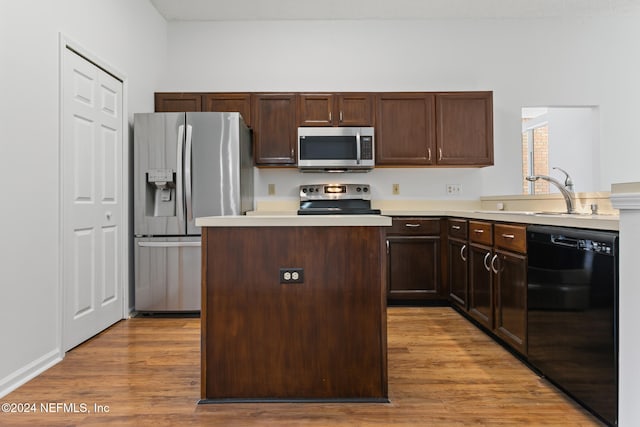 kitchen featuring stainless steel appliances, light countertops, light wood-style flooring, a sink, and a kitchen island