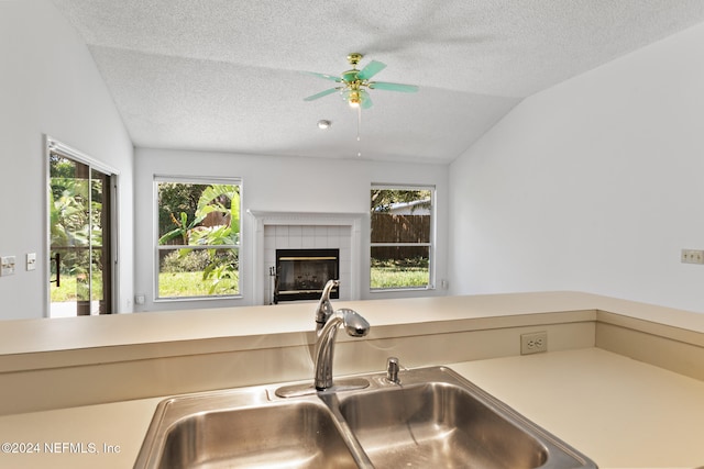 kitchen featuring a tiled fireplace, lofted ceiling, open floor plan, a textured ceiling, and a sink