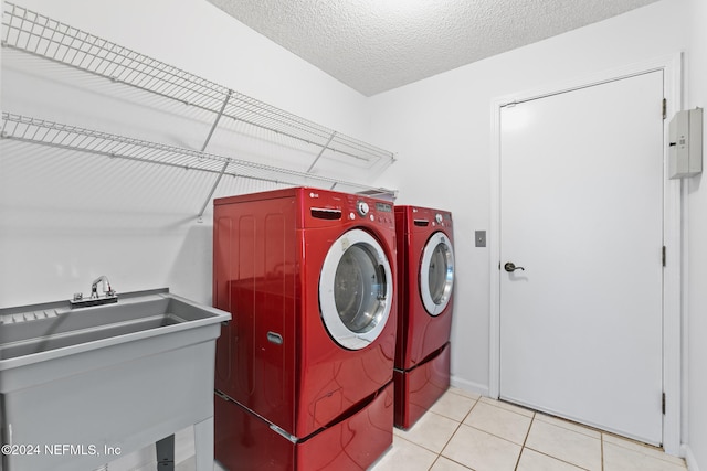 laundry area featuring washing machine and dryer, light tile patterned flooring, a sink, a textured ceiling, and laundry area