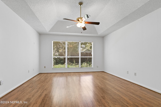 unfurnished room featuring a textured ceiling, ceiling fan, wood finished floors, baseboards, and a tray ceiling