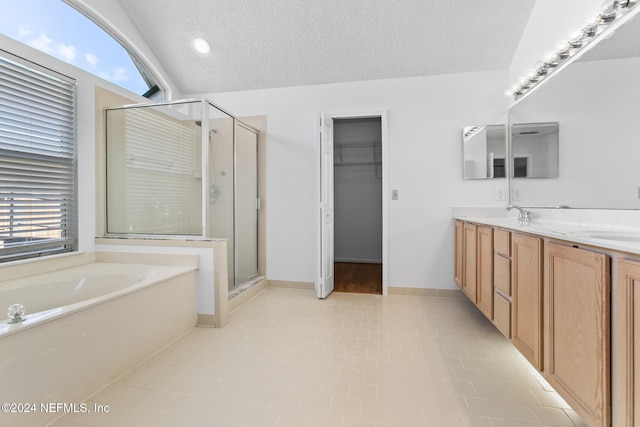 full bath with a textured ceiling, a shower stall, a bath, double vanity, and a walk in closet