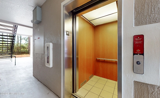 hallway featuring tile patterned floors, a textured ceiling, and elevator