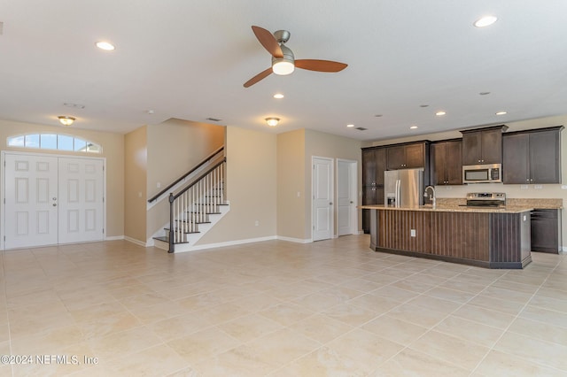 kitchen with sink, dark brown cabinets, appliances with stainless steel finishes, light stone countertops, and a kitchen island with sink