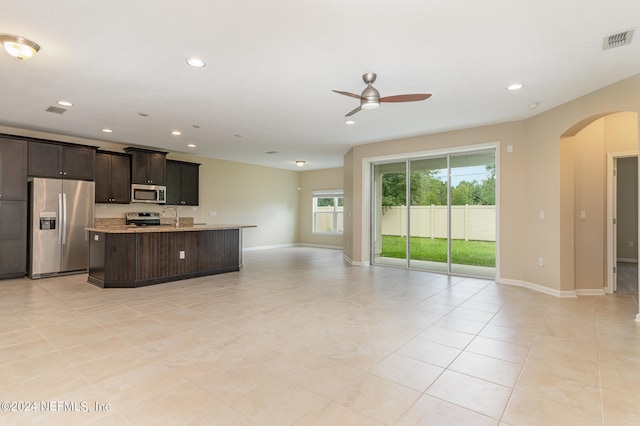 kitchen with a center island with sink, light tile patterned floors, stainless steel appliances, ceiling fan, and sink