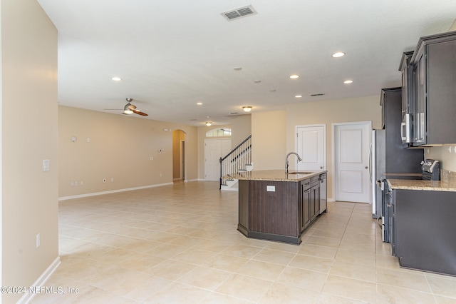 kitchen with a center island with sink, light stone counters, stainless steel fridge, ceiling fan, and sink