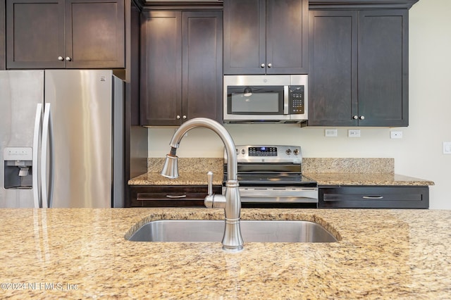 kitchen featuring stainless steel appliances, dark brown cabinets, sink, and light stone counters