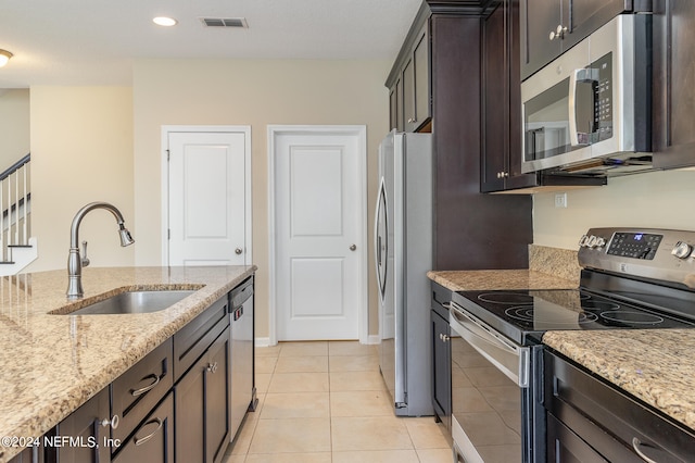 kitchen with light tile patterned floors, appliances with stainless steel finishes, dark brown cabinets, sink, and light stone counters