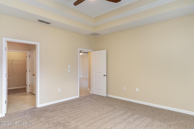 unfurnished bedroom with ceiling fan, a closet, a walk in closet, and light colored carpet