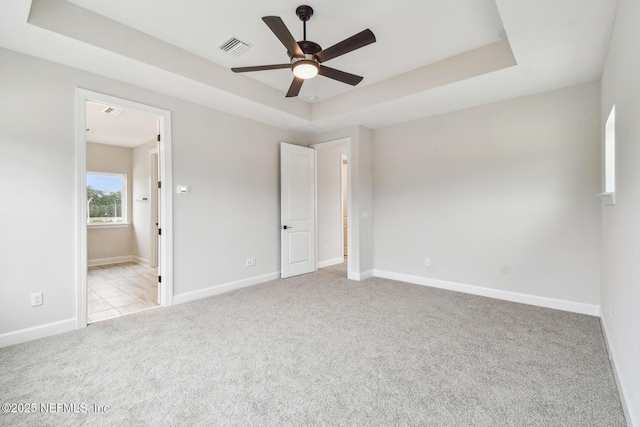 unfurnished bedroom featuring light carpet, a tray ceiling, ceiling fan, and ensuite bathroom